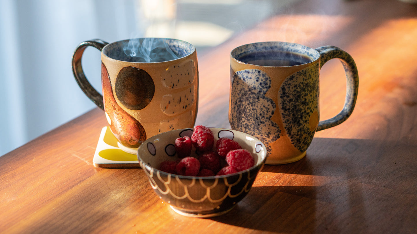 lifestyle shot of two handmade cups on wooden table by a hill studio